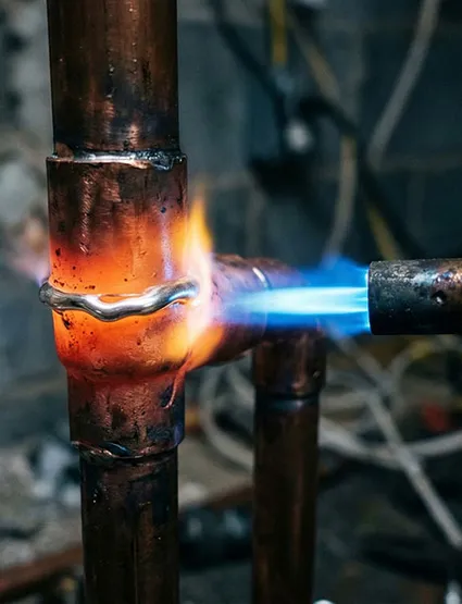 Propane torch brazing a copper pipe joint during a heating system installation